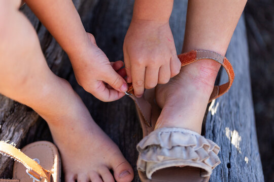 Child doing up buckles on sandal shoes while sitting on log outdoors