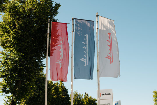 Flags of a car dealership moskvich are flying in the wind outside a location in daytime. setting features clear weather with bright sky and trees in the background Smolensk, Russia 07.17.2026