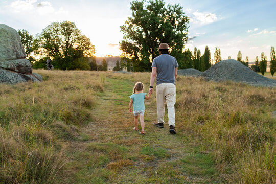 Dad on walk with young daughter walking away down grassy path in recreational area