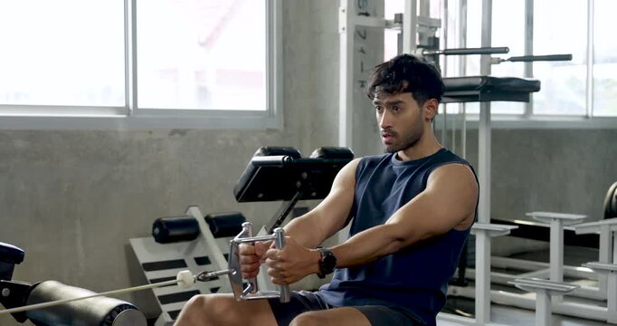 Young Asian man trains alone on seated cable row machine in modern gym, pulling handle toward torso with steady rhythm, upper body strength workout, muscle building, wellness, healthy lifestyle.