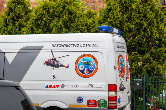 White aeronautical search and rescue ASAR van with specialized markings and helicopter stickers parked by a green fence and thuja trees during operation.
