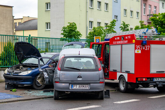Crashed passenger cars Peugeot and Opel Corsa with open engine hoods next to red fire truck of OSP Borkow Stary during city accident.