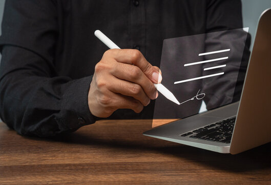 Person signing digital document with stylus beside laptop