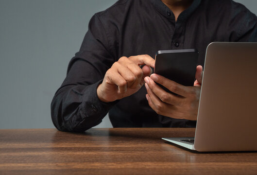 Person using smartphone beside laptop at wooden desk