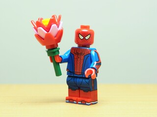 Naklejka premium Indonesia - May 27, 2026 : Mini toy of action figure at outdoor with blur background. Miniature photography concept design. Minifigure of Spiderman character hold bouquet of flower. Romantic person.