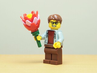 Fototapeta premium Indonesia - May 27, 2026 : Mini toy of action figure at outdoor with blur background. Miniature photography concept design. Minifigure of man character hold bouquet of flower. Romantic person.