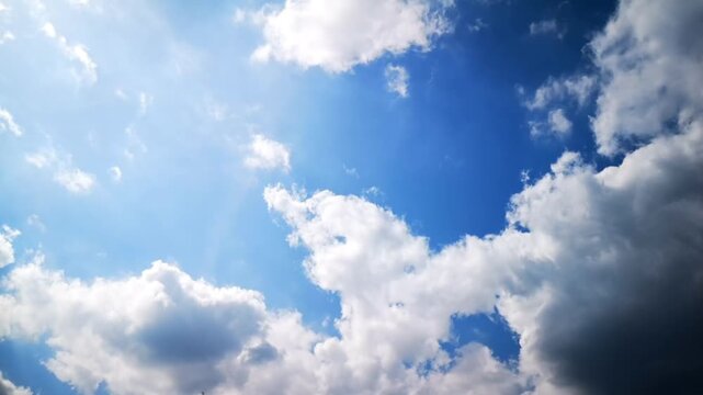 The beauty of a bright blue daytime sky. Masses of white cumulus clouds are visible, moving rapidly in the wind and contrasting with the somewhat darker clouds in the bottom right corner. 