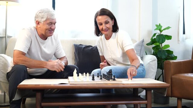 The elderly family, including the grandparents, were relaxing, playing chess together, and chatting in the living room of their house. 