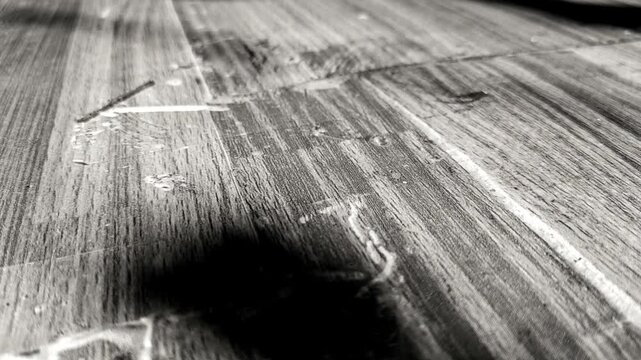 Moody black and white footage of vertical moving shadow lines from a window casting over a rustic wooden floor texture, abstract cinematic background loop.