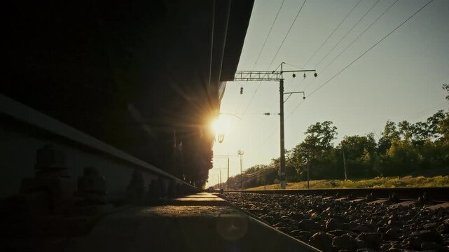 On sunlit railway track, freight train speeds past as its wheelsets glide over sleeper rails. The close-up view underscores railway infrastructure and routine track maintenance in open field settings