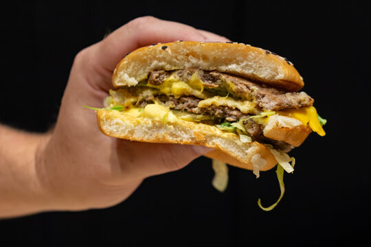 Male hand holding a delicious double cheeseburger with melted cheese and lettuce on black background