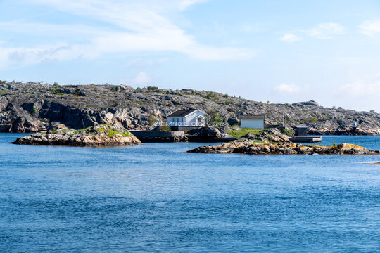 Tranquil Scandinavian rocky coastal landscape featuring a traditional white house by the deep blue sea. Ideal for travel and real estate concepts.