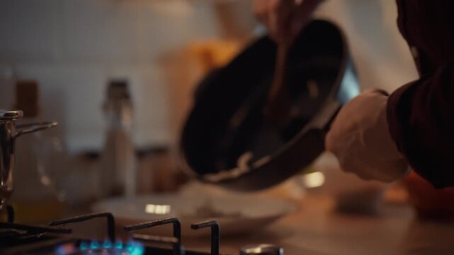 A man carefully places crispy fried onions from a hot pan onto a waiting dinner plate, finalizing a cook's key step in preparing a savory evening meal