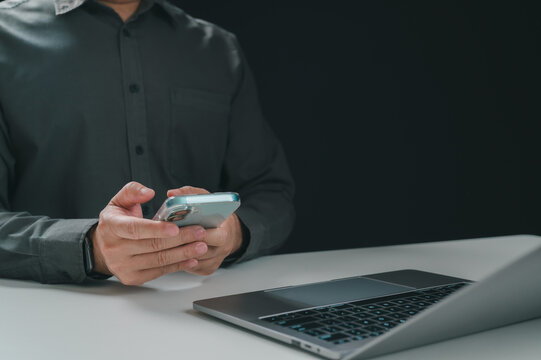 Man using a smartphone next to a laptop on a dark background