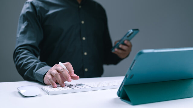 Man using a keyboard and tablet while holding a smartphone
