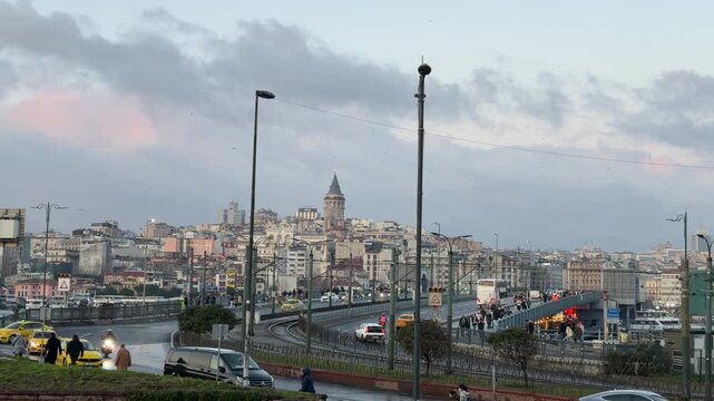 Wide angle shot capturing the bustling cityscape and iconic Galata Tower at sunset with flowing traffic on the Galata Bridge in Istanbul, Turkey.