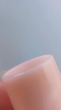 Close up front view of clear lip balm with pink packaging slowly coming out from the tube. Beauty cosmetic product, glossy texture for lip care concept.