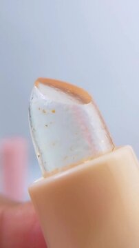 Close up front view of transparent lip balm with yellow packaging rotating slowly. Soft blurred white background. Beauty cosmetic product concept.