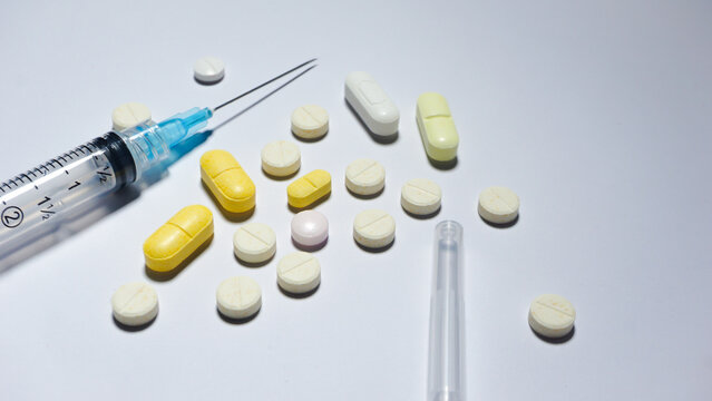 White and yellow pills with a syringe on white surface. Medical concept.