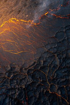 Aerial top down view of cooling lava flow with glowing orange cracks and dark volcanic crust, abstract geological pattern of volcanic eruption