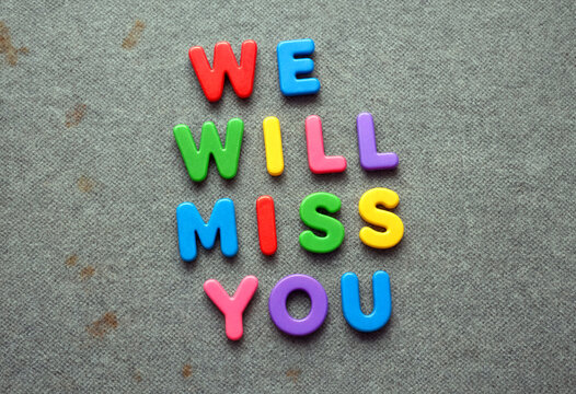 Colorful plastic letters spelling we will miss you on a textured gray fabric background