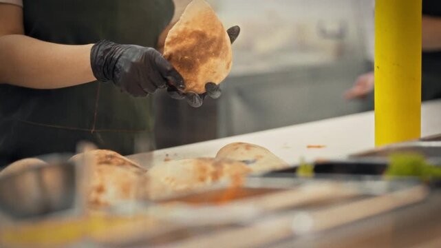 A close-up of a gloved chef using a knife to cut a bun and fill it with meat and vegetables. Concept for a fresh takeaway sandwich and professional street food preparation