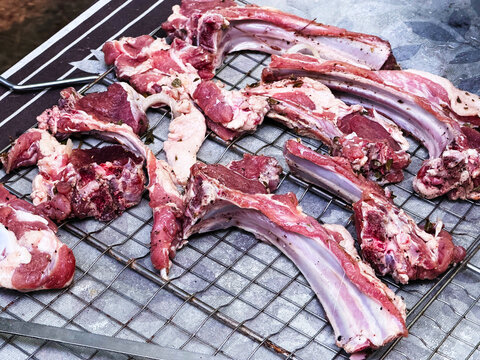 Raw lamb ribs and pieces of meat laid out on a metal grill before cooking. Fresh lamb with a natural texture is ideal for cooking shish kebab, barbecue, grill and traditional meat dishes. The photo
