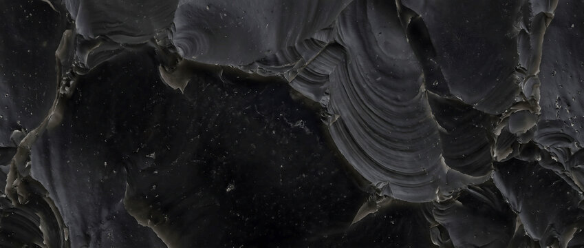 Black stone texture displaying a polished obsidian flint mineral surface with sharp glasslike fractures provides a luxury natural backdrop for premium design layouts