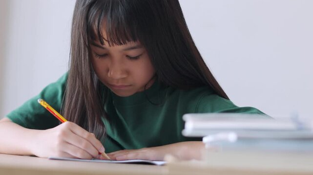 Selective focus portrait of an Asian kid improving her writing skills. The young student is focused on her textbook assignment, representing homeschooling, diligent study, and modern education.