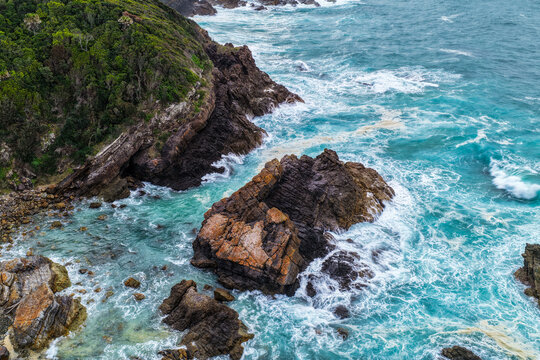 Aerial view of powerful waves breaking across rugged rock formations, creating swirling whitewash along the coastline at Burgess Beach, Forster on the Mid North Coast of NSW.