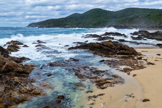 Aerial view of powerful waves breaking across rugged rock formations, creating swirling whitewash along the coastline at Burgess Beach, Forster on the Mid North Coast of NSW.