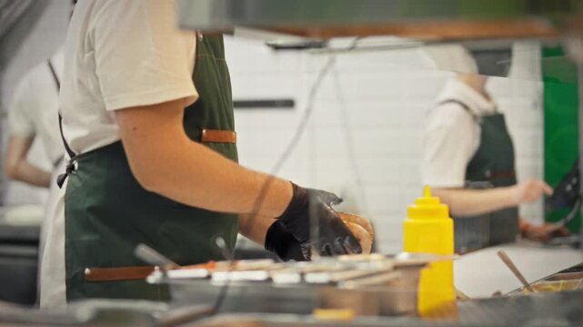 A chef in an apron and gloves adds sauce to a pita with prepared meat and vegetable fillings. Concept of the final touch in preparing fresh pita for takeout
