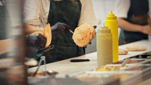 A chef in an apron expertly fills a fresh pita with meat and vegetable fillings while preparing an order. A concept for a small business and professional street food preparation for customers