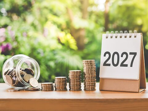 Stacks of coins in ascending order with a glass jar of money and a flip calendar showing 2027 year signifying financial growth savings and investment planning for the upcoming year.