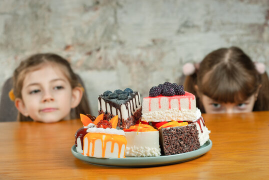 Two children looking at a plate of desserts placed on a wooden table in a casual setting