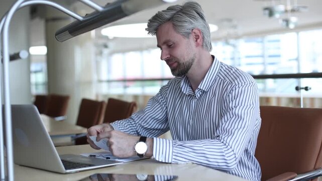Young businessman sitting at a table at modern office working on a computer and opening envelope