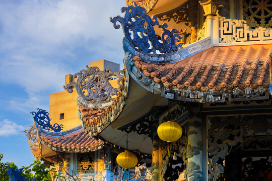The traditional multi-tiered roof of a Chua Tan Thai Pagoda with curved corners is adorned with decorative mosaics, red tiles, intricate stone carvings and chinese lanterns at Da Nang, Vietnam