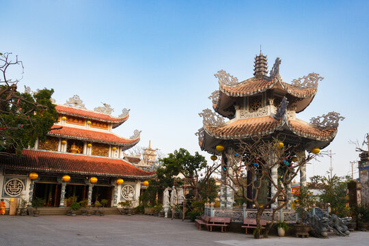 A spacious courtyard of a Chua Tan Thai Pagoda with a traditional multi-tiered pavilion with a large bell and the main building of the sanctuary at Danang, Vietnam