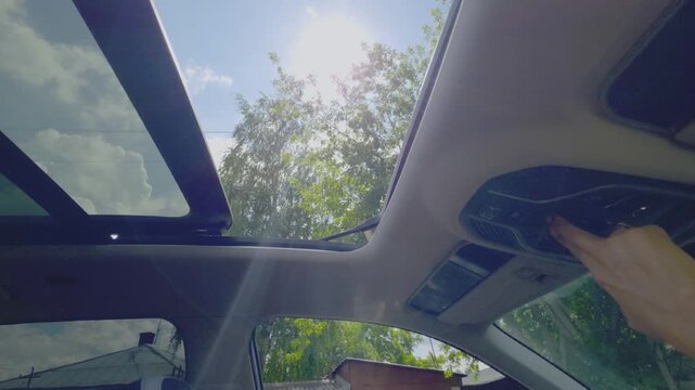 Woman finger pushes button to close vehicle sunroof. Modern car ceiling panel glass slides shut to block bright sunlight. Driver operating panoramic roof system.