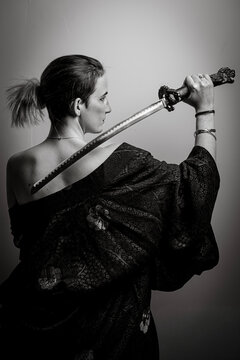 Artistic black and white studio portrait of a powerful woman in a kimono holding a katana sword over her shoulder