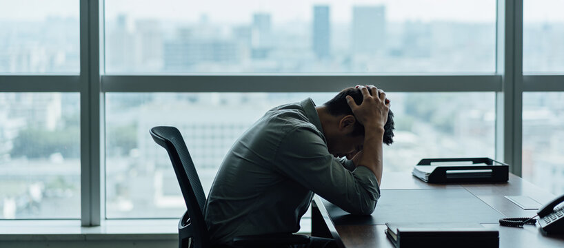 Man sitting at his desk with his head in his hands, representing workplace stress and mental fatigue