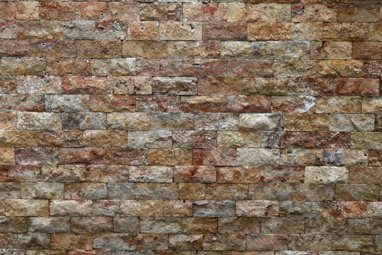 Rustic textured travertine stone wall background with decorative brick tiles.