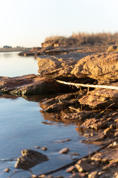 Sunlight glows over calm water beside rugged, weathered rocks