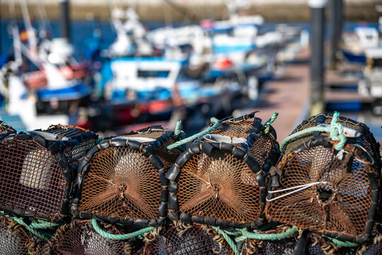 Traditional Stacked Fishing Traps on the Pier of a Galician Harbor with Trawlers Docked in Northern Spain