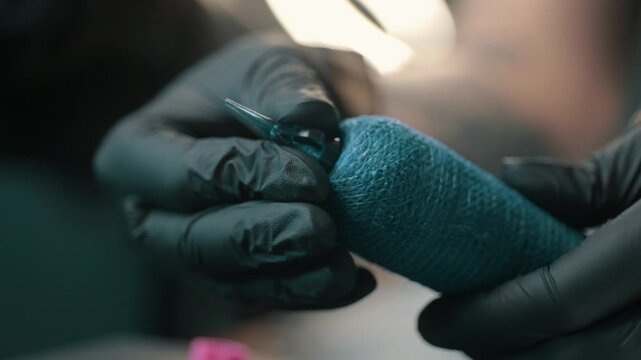 Close-up of a tattoo artist wearing black gloves preparing a tattoo machine with blue grip tape before a professional tattooing session.