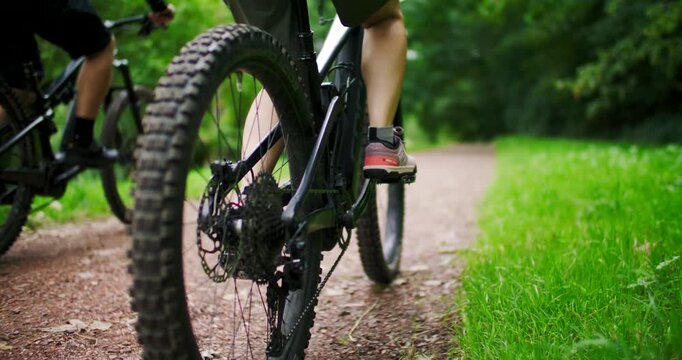 Close up of mountain bike wheels and pedaling legs on forest trail