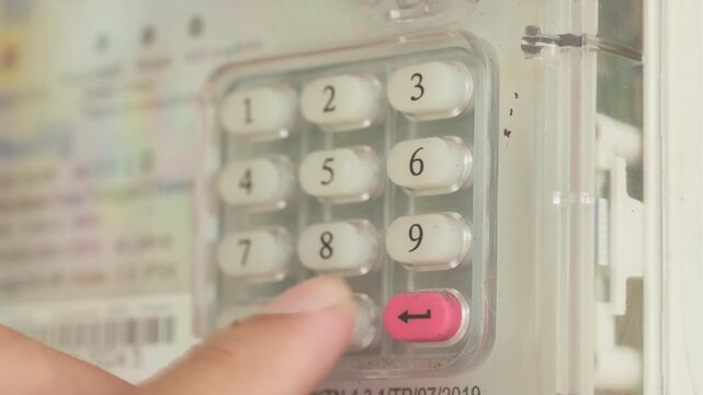 Hand pressing buttons on keypad of home electricity meter