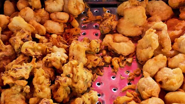 Traditional Indonesian fried snacks displayed at a street food stall while a vendor selects fresh fritters for customers. Authentic local cuisine featuring crispy homemade snacks and vibrant street fo