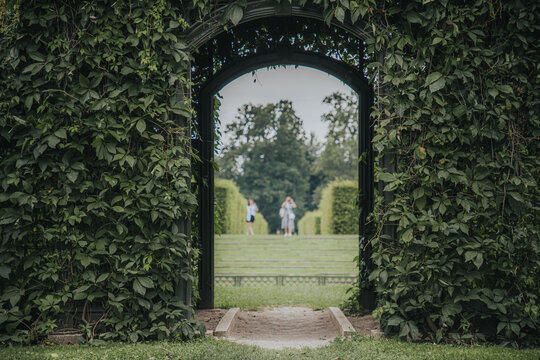 Rundale, Latvia - July 18, 2026: Archway covered in green vines leading to a manicured garden with people walking in the distance under a cloudy sky