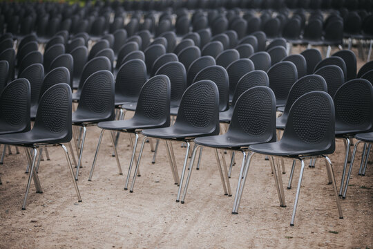 Rows of black plastic chairs with chrome legs arranged neatly on a dirt ground, ready for an outdoor event or gathering in a spacious area